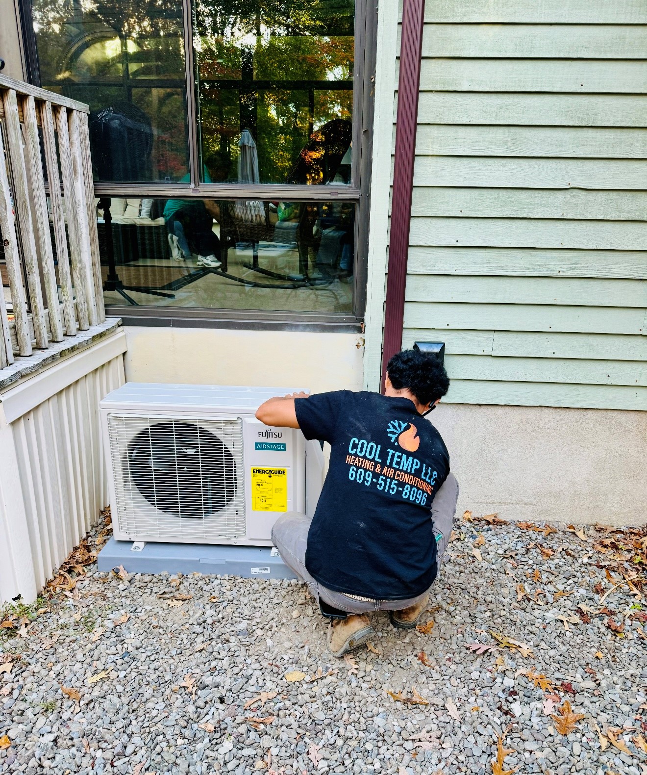 A person installs or checks an outdoor air conditioning unit next to a building with a window and siding.